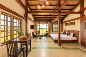 A room with a bed, a dining table with chairs, a small table with a bowl of fruit, and a view of the outdoors. - Sola Hoi An (Da Nang Municipality)