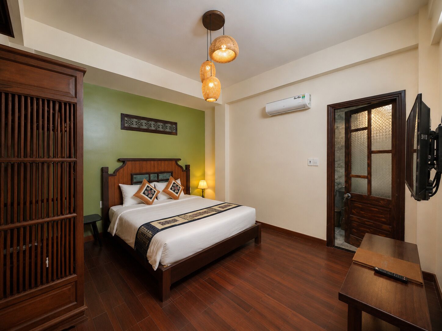 A hotel room with a wooden bed, a nightstand, a wall-mounted air conditioner, and a door with a frosted glass panel.