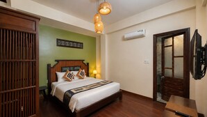 Una habitación de hotel con una cama de madera, una mesita de noche, aire acondicionado instalado en la pared y una puerta con un panel de vidrio esmerilado.