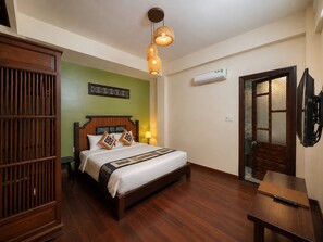 A hotel room with a wooden bed, a nightstand, a wall-mounted air conditioner, and a door with a frosted glass panel. - Sola Hoi An (Da Nang Municipality)