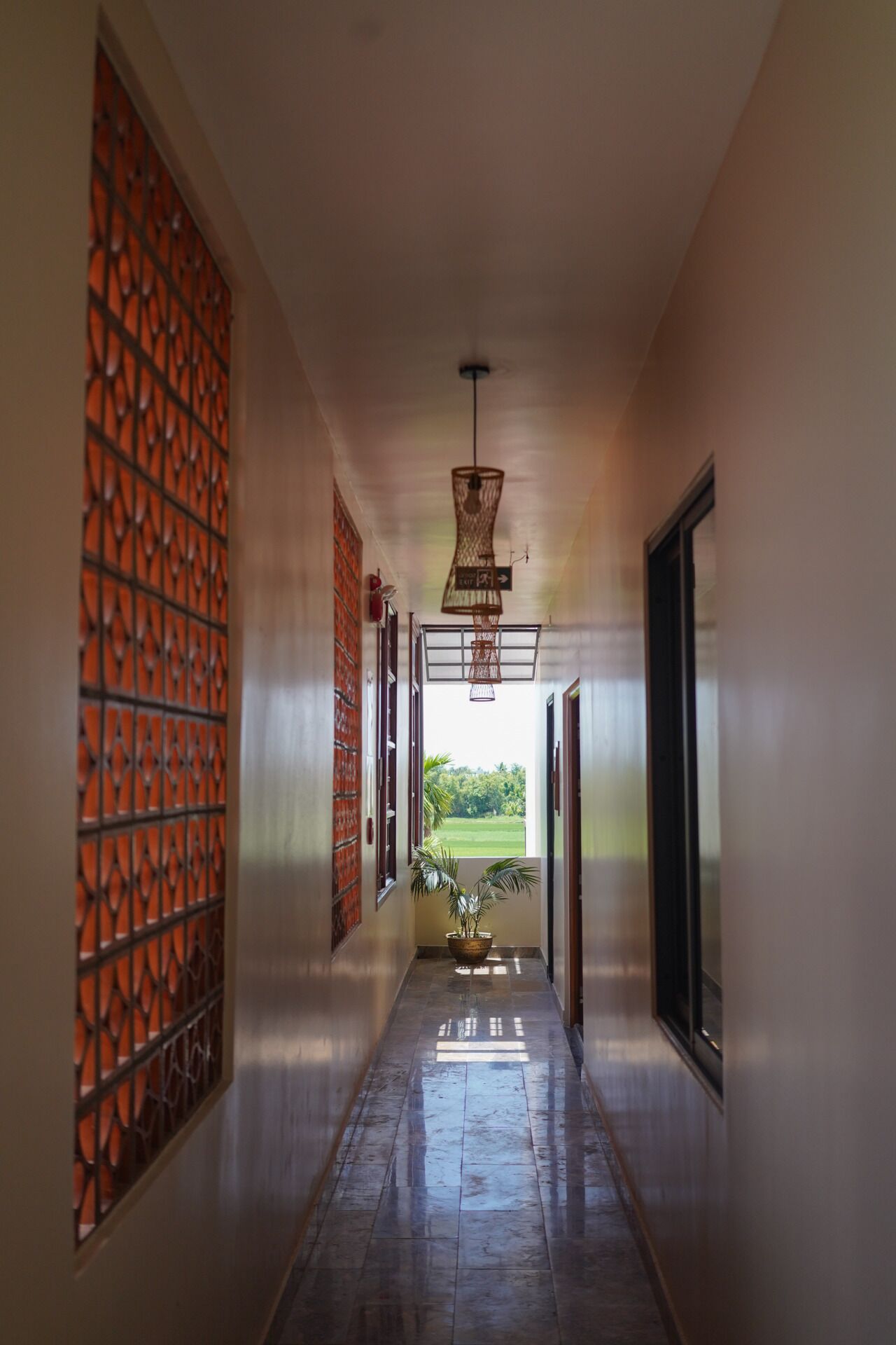A hallway with a view to a garden, a hanging light fixture, and a potted plant.