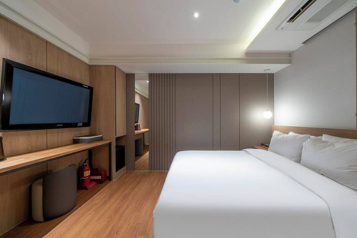 A modern hotel room with a large bed, a flat-screen TV, a desk with a computer, and a wardrobe.