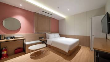 A modern hotel room with a bed, bedside table, a round mirror, a small table, and a television.