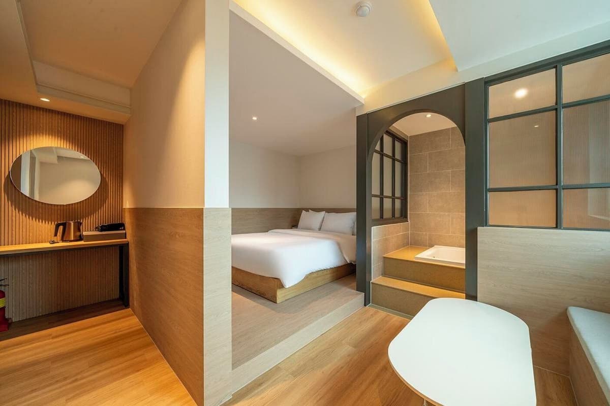 A modern hotel room with a bed, a desk, a chair, and a bathroom with a bathtub.