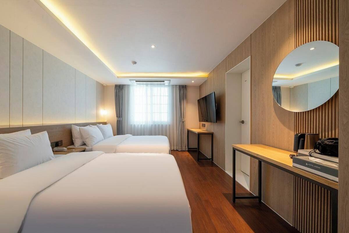 A hotel room with two beds, a TV, a desk, a mirror, and a window with curtains.