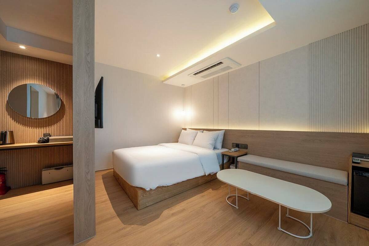 A modern hotel room with a bed, bedside table, bench, and a mirror.