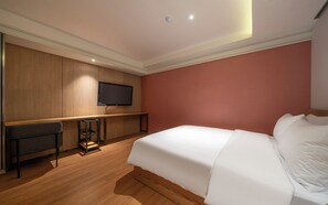A hotel room with a bed, a TV mounted on a wooden panel wall, a small table, and a chair. - Busan Yongho-dong Athena Hotel (Busan)