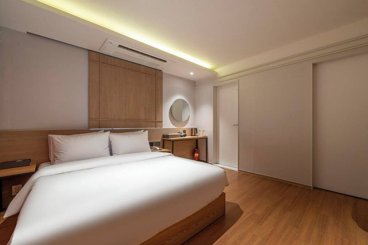 A hotel room with a large bed, bedside table, a round mirror, a wardrobe, and a door.