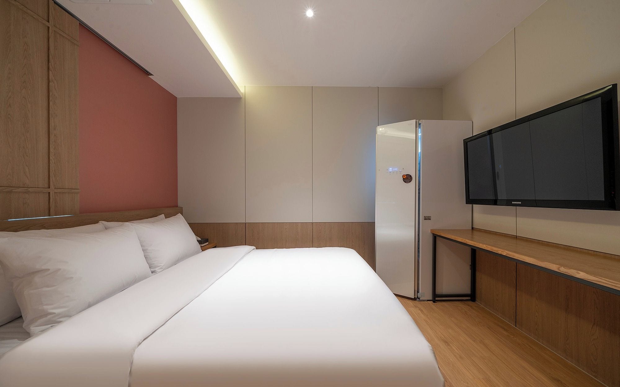 Una habitación de hotel moderna con una cama grande, un televisor de pantalla plana en la pared y un armario empotrado.