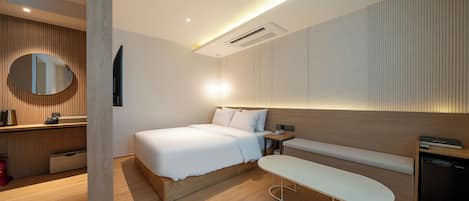 A modern hotel room with a bed, bedside table, and a small desk with a chair.