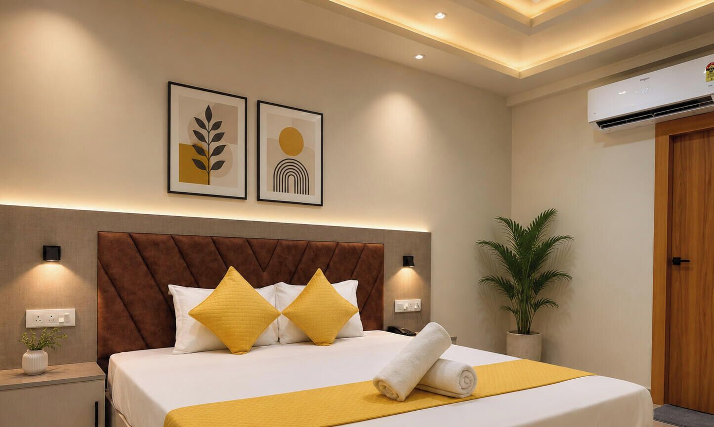 A hotel room with a bed, bedside lamps, a potted plant, and artwork on the wall.