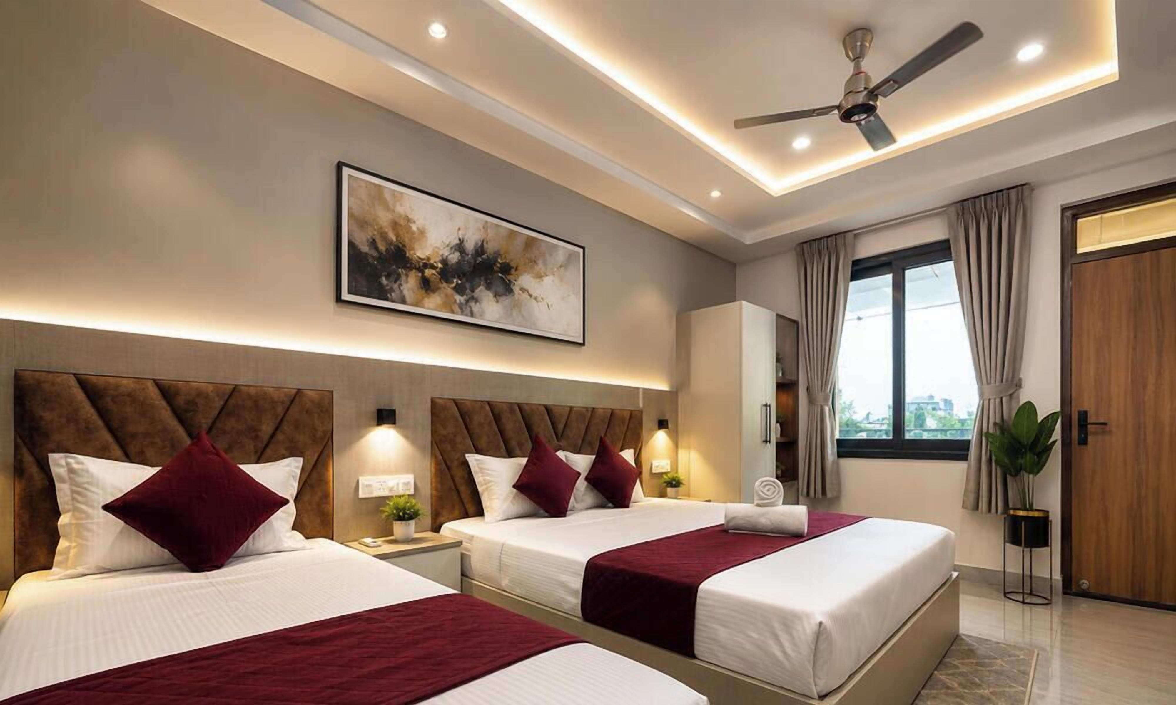 Une chambre d’hôtel avec deux lits, un ventilateur de plafond, un grand tableau abstrait et une vue sur la ville par la fenêtre.