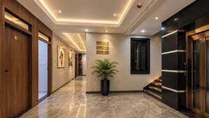 Un couloir d’hôtel avec des portes en bois, une plante en pot, des panneaux de signalisation et un sol en marbre.