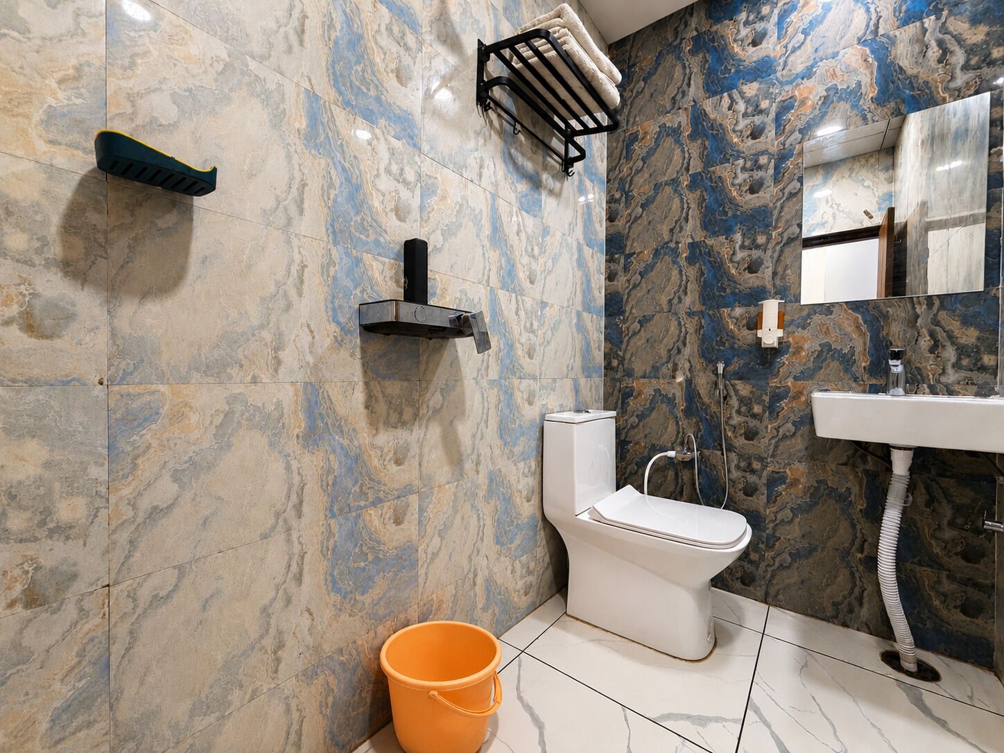 A bathroom with a toilet, sink, and shower. There is a towel rack and a bucket on the floor.