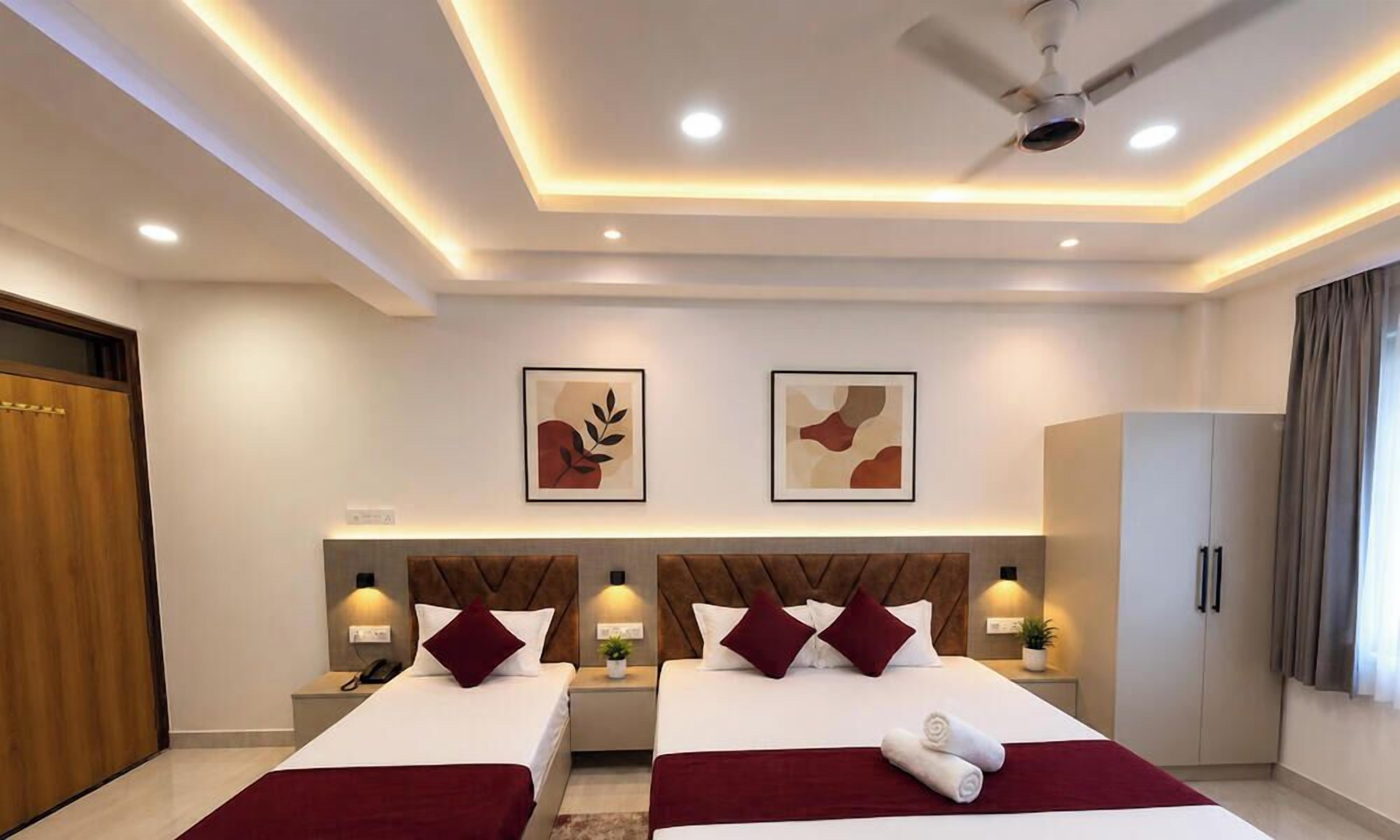 Une chambre d’hôtel moderne avec deux lits, un ventilateur de plafond, un éclairage encastré, des œuvres d’art aux murs et une armoire.