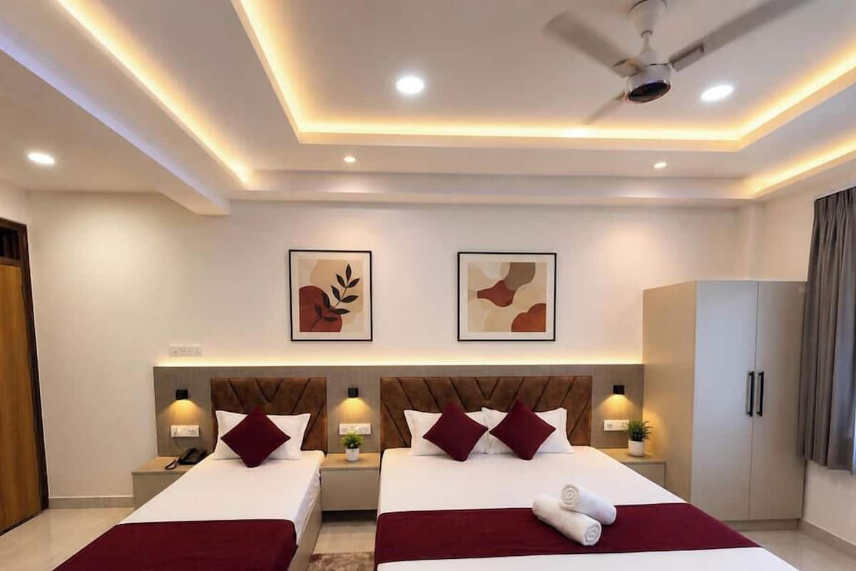 A modern hotel room with two beds, a ceiling fan, recessed lighting, artwork on the walls, and a wardrobe.