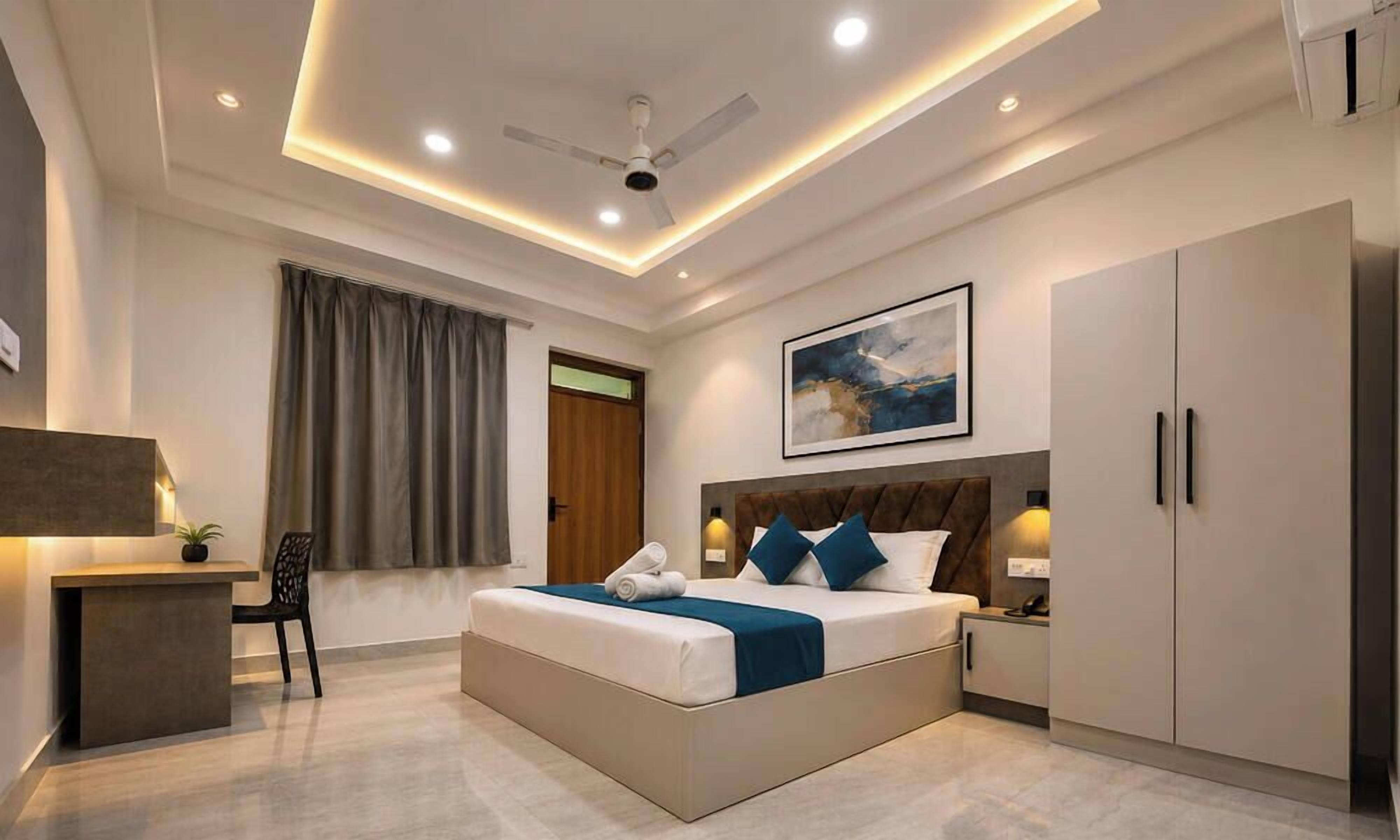 Une chambre d’hôtel moderne, dotée d’un grand lit, d’un bureau, d’une chaise, d’un ventilateur de plafond et d’un tableau au mur.