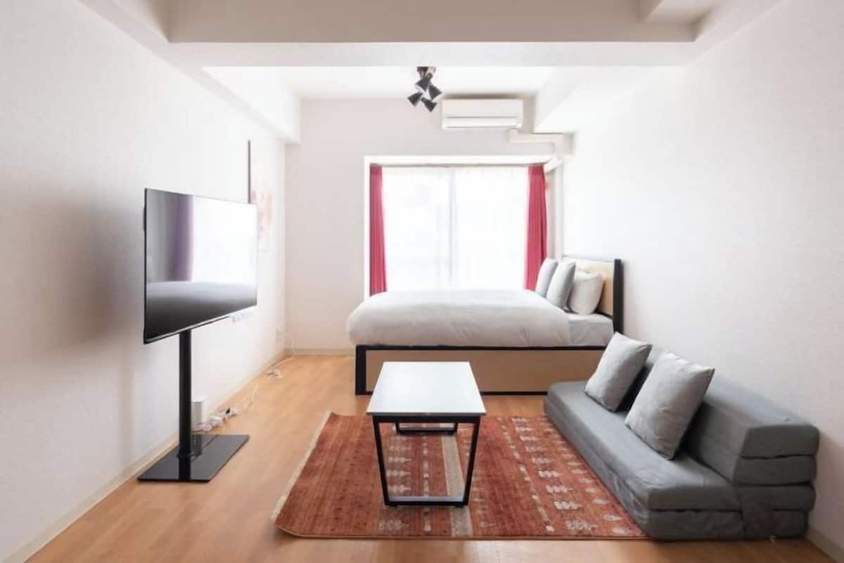 A modern room with a bed, a TV, a small table, and a sofa.