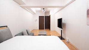 A modern hotel room with a bed, a television, a small seating area, and a door leading to a bathroom. - AXIA (Osaka)