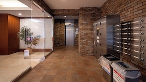 A lobby with a glass partition, a brick wall, a trash bin, and a set of lockers. - AXIA (Osaka)