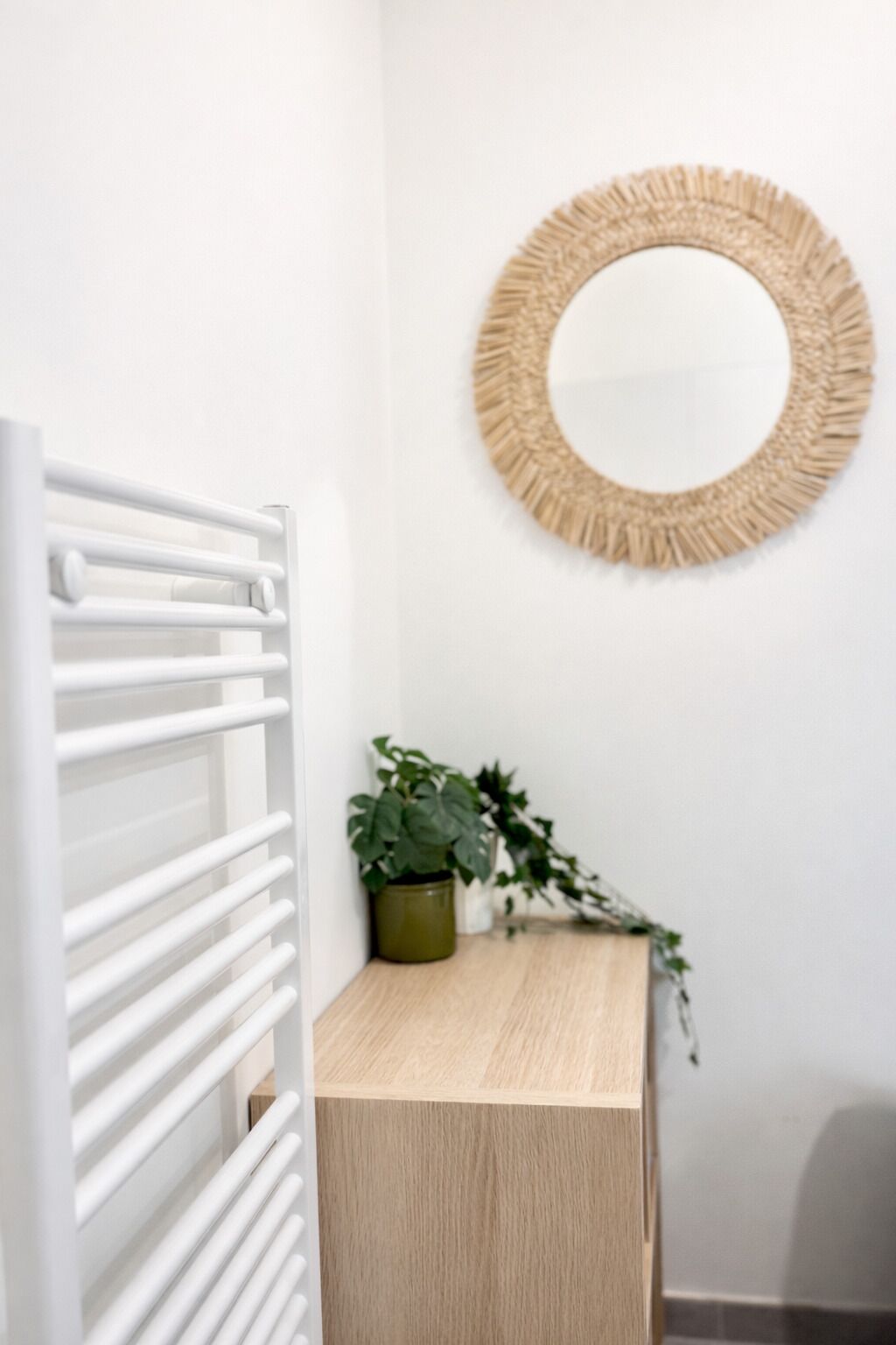 Eine weiße Heizung, ein Holzschrank, ein Blumentopf und ein gewebter Spiegel an der Wand.