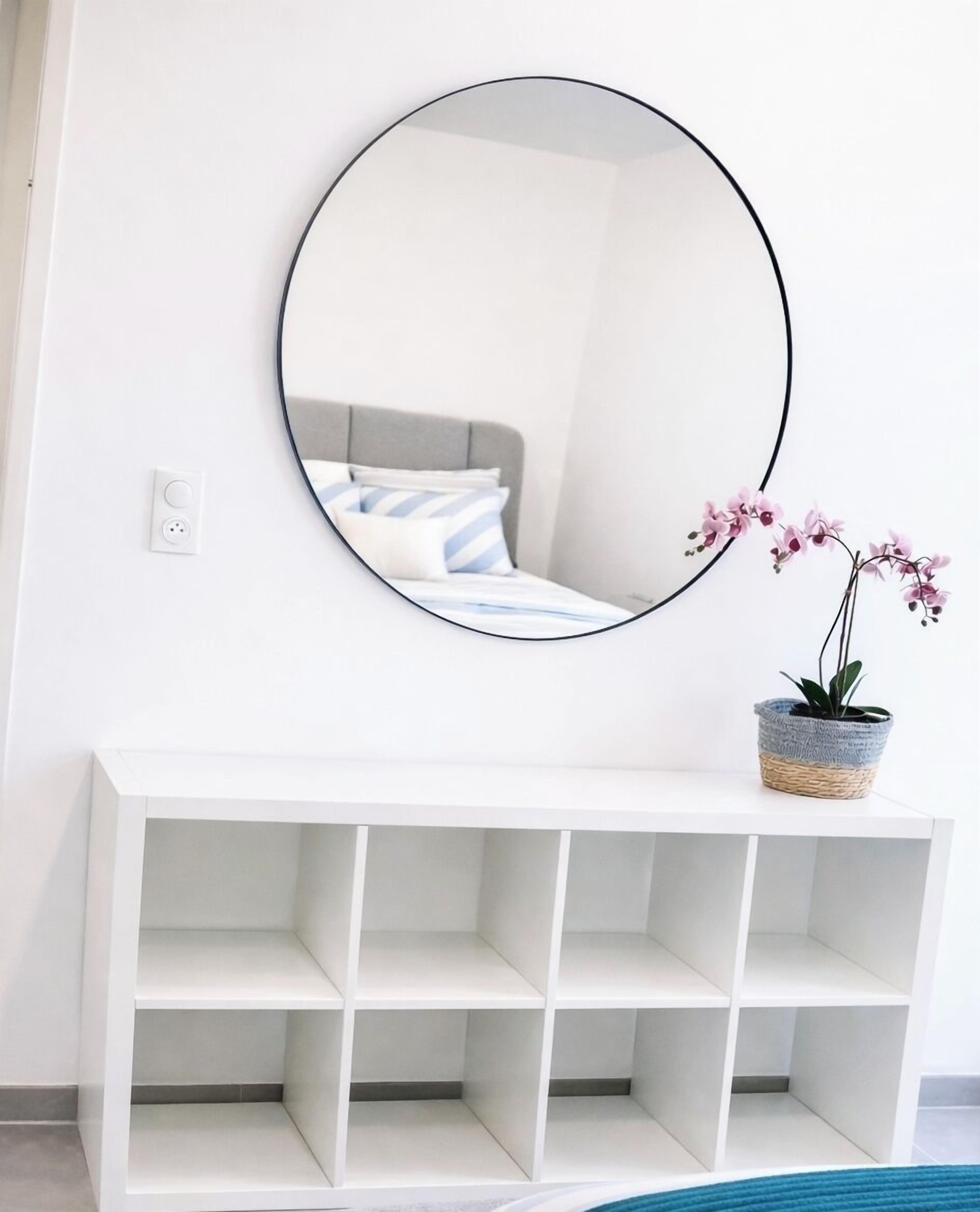 Ein weißes Konsolenbett mit grauem Kopfteil, ein runder Spiegel an der Wand und ein Blumentopf auf der Konsole.
