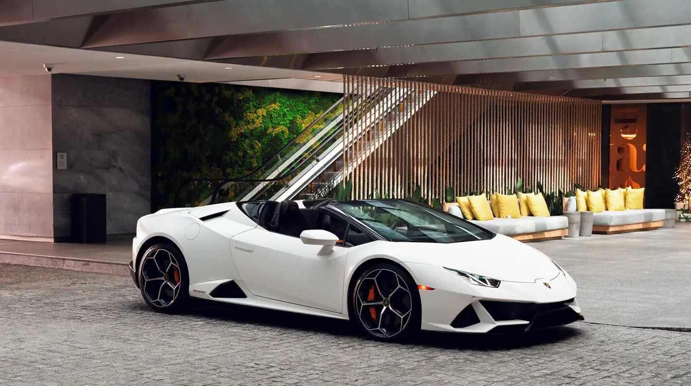 Een witte sportauto geparkeerd in een moderne hal met een trap, een bank met gele kussens en een groene wand.
