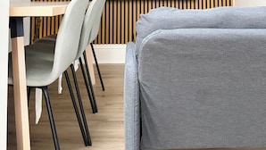 Ein modernes Wohnzimmer mit Flachbildfernseher, einer Wand aus Holzlamellen, einem Esstisch mit Stühlen und einem grauen Sofa.