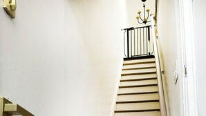 Eine Treppe mit weißen Wänden, einem schwarzen Geländer und einer Kandelaberbeleuchtung oben.