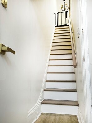 Eine Treppe mit weißen Wänden, einem schwarzen Geländer und einer Kandelaberbeleuchtung oben.