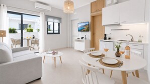 Uma sala de estar moderna com um sofá, uma mesa de jantar para dois e uma área de cozinha com armários brancos e uma televisão.