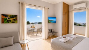Quarto de hotel com varanda, uma cama, um sofá, uma mesa pequena e uma televisão.