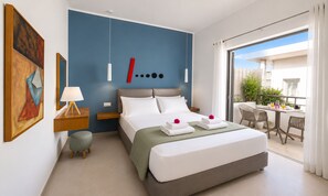 A modern hotel room with a large bed, a balcony with a table and chairs, and a view of greenery.