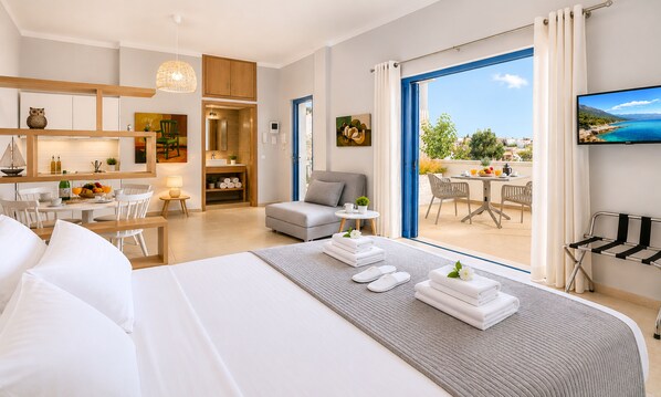 A hotel room with a bed, a dining area, a kitchen, and a balcony with a view.
