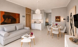A modern living space with a sofa, dining table, chairs, a kitchen area, and artwork on the walls. - Art Apartments (Palaiochora)
