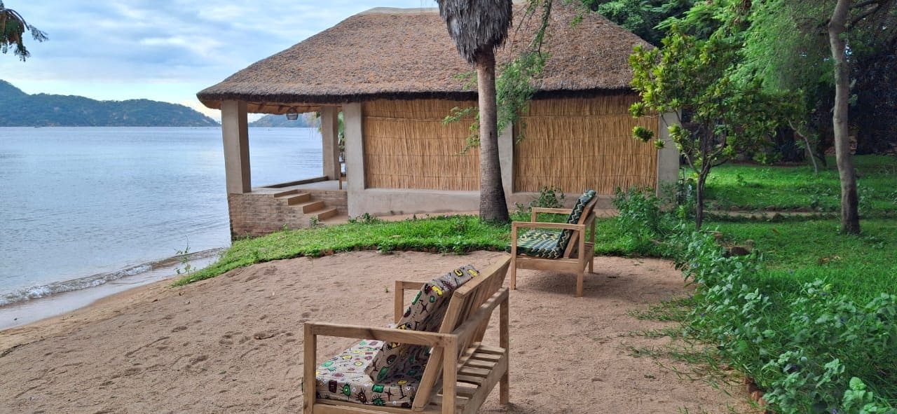 Uma cabana à beira-mar com telhado de palha, cadeiras de madeira e vista para a água.