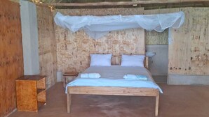 A wooden bed with a canopy, a nightstand, and a small wooden table. - Anake Lodge (Cape Maclear)