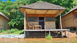 A thatched-roof hut with a wooden porch, a chair, and a table. - Anake Lodge (Cape Maclear)