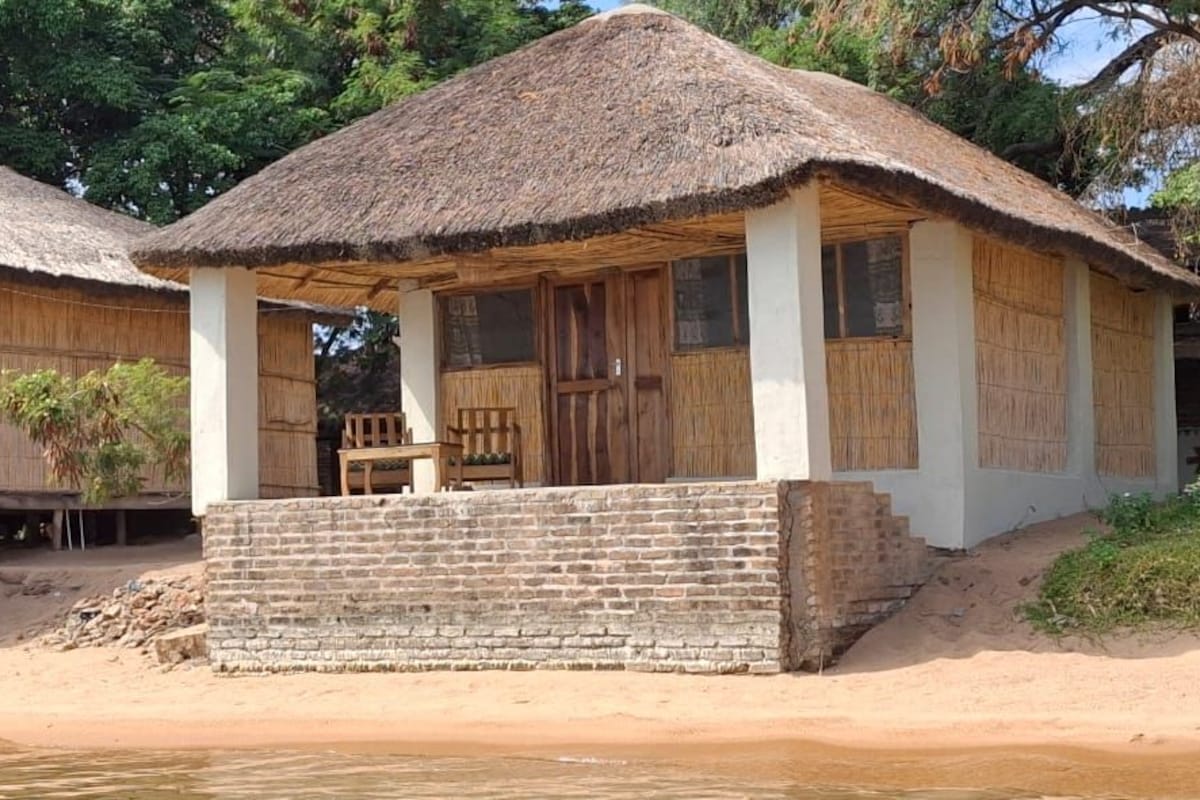 Une cabane à toit de chaume, dotée d’un porche en bois et d’une fondation en briques.