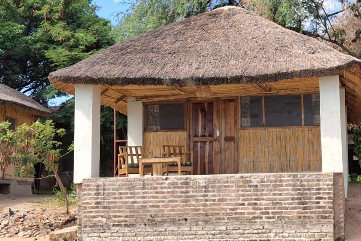 Une cabane rustique avec un toit de chaume, des murs en bois et un banc à l’extérieur.