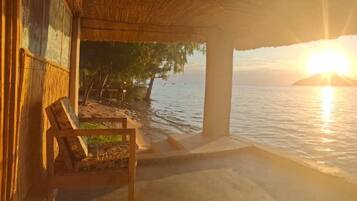A beachside view with a wooden chair and a thatched roof structure.