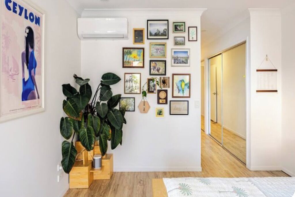 Una habitación con aire acondicionado de pared, una planta en maceta y una colección de cuadros enmarcados.