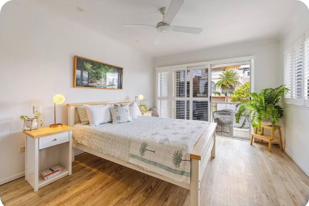 Een slaapkamer met een bed, nachtkastjes, een plafondventilator, een raam met luiken en uitzicht op de omgeving.