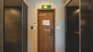 A hotel elevator with a wooden door, a 'NO SMOKING' sign, and a 'TAKE YOUR KEY CARD' instruction.