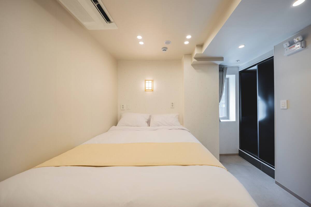 A bedroom with a bed, a bedside table, a window, and a door.