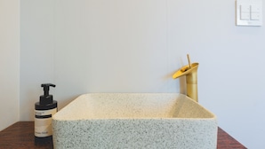 A bathroom with a rectangular sink, a bottle of soap, and a gold-colored object on the counter.