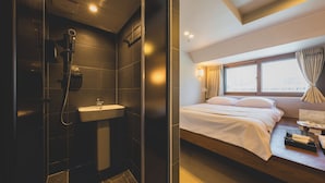 A modern hotel room with a shower, sink, and a bed with a window view.