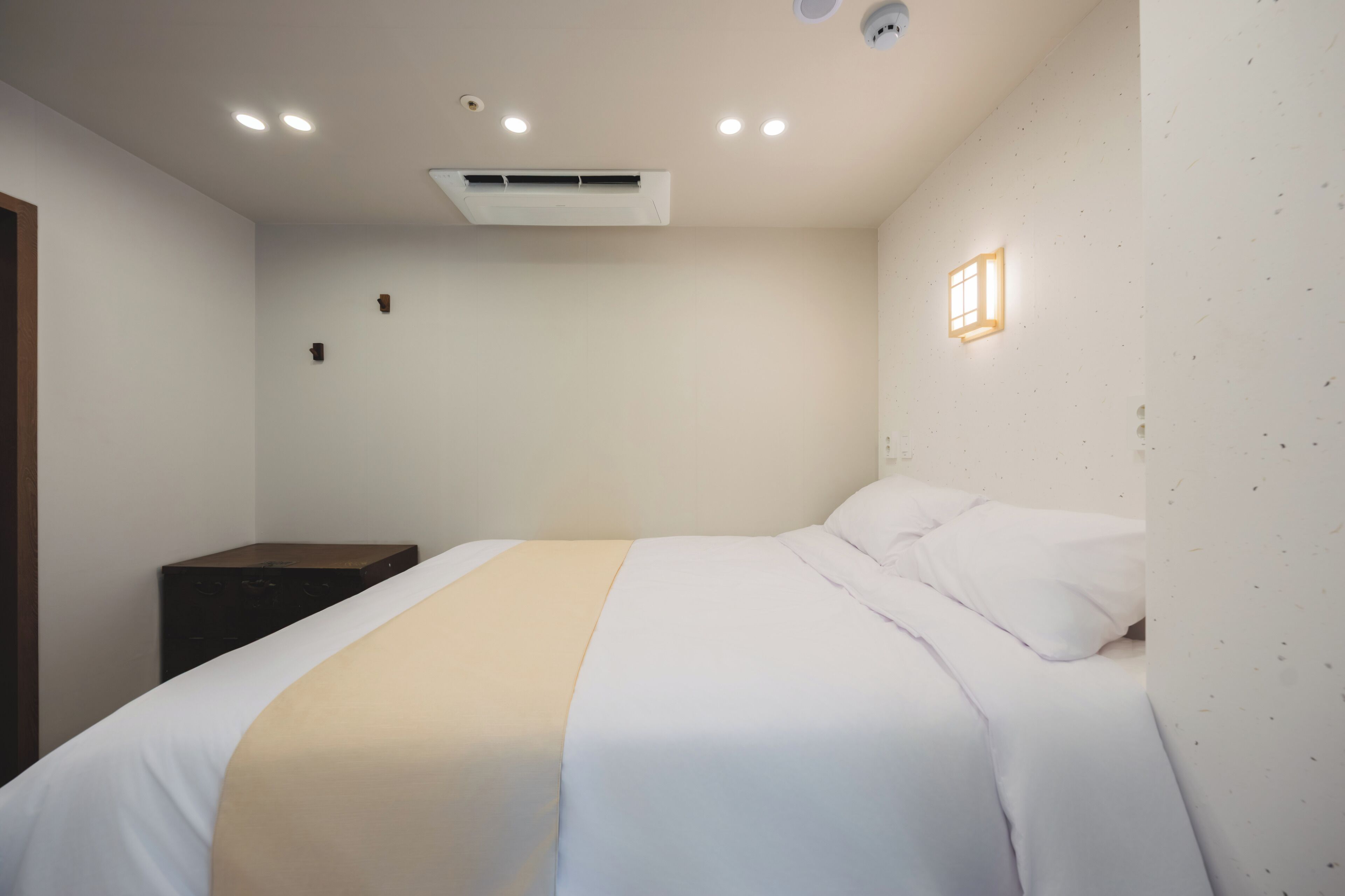 Un dormitorio con cama, mesita de noche, lámpara de pared y unidad de aire acondicionado.