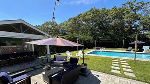Un patio exterior con piscina, sillas de descanso y un área de estar cubierta.