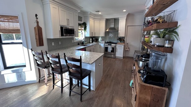 Una cocina moderna con armarios blancos, una isla central, sillas de madera y electrodomésticos integrados.